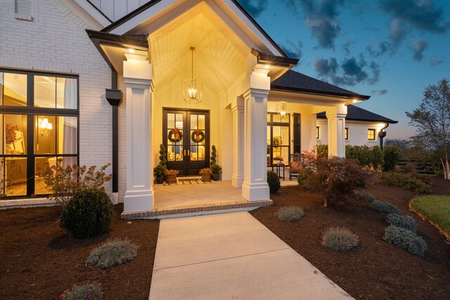 property entrance with brick siding, a shingled roof, and french doors