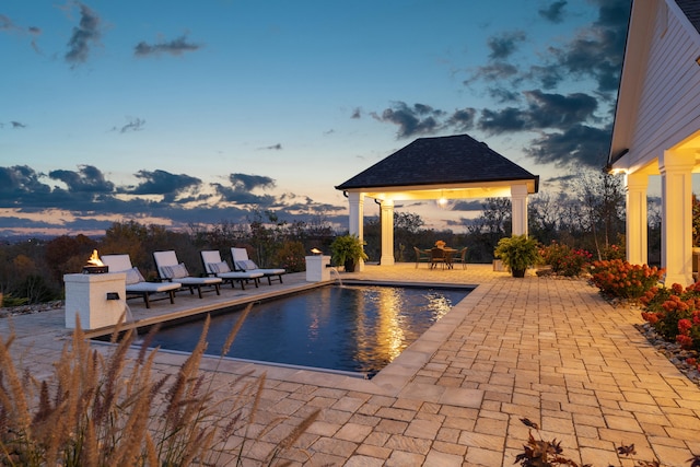 pool at dusk featuring a gazebo, a patio, and an outdoor pool