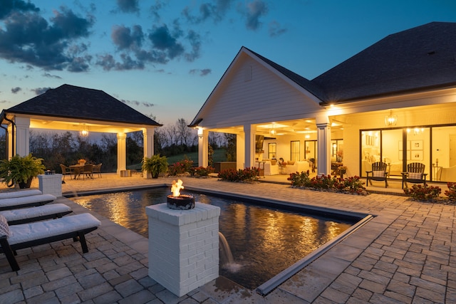 pool at dusk featuring a gazebo, an outdoor fire pit, a patio area, and an outdoor pool