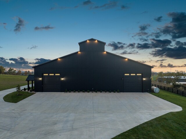 property exterior at dusk featuring a garage, driveway, fence, and a lawn