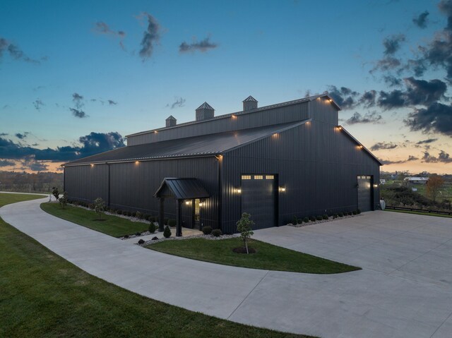 property exterior at dusk featuring metal roof, concrete driveway, a lawn, and a garage