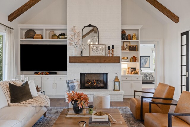 living area with a fireplace, high vaulted ceiling, wood finished floors, and beamed ceiling