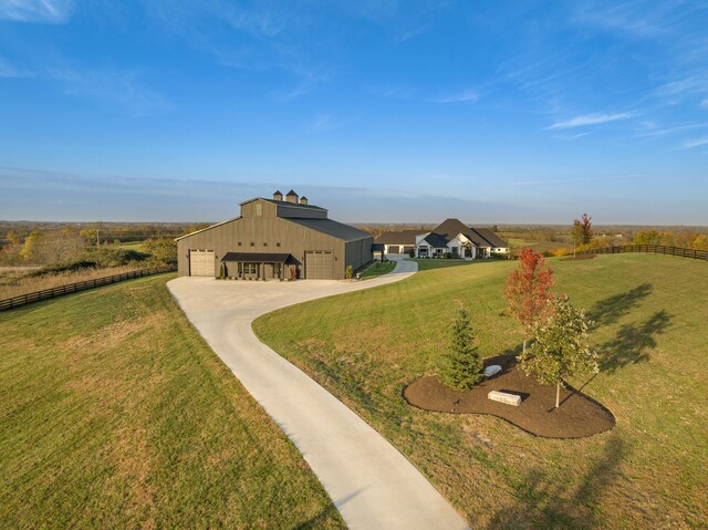 view of property's community featuring a yard, a rural view, concrete driveway, and fence