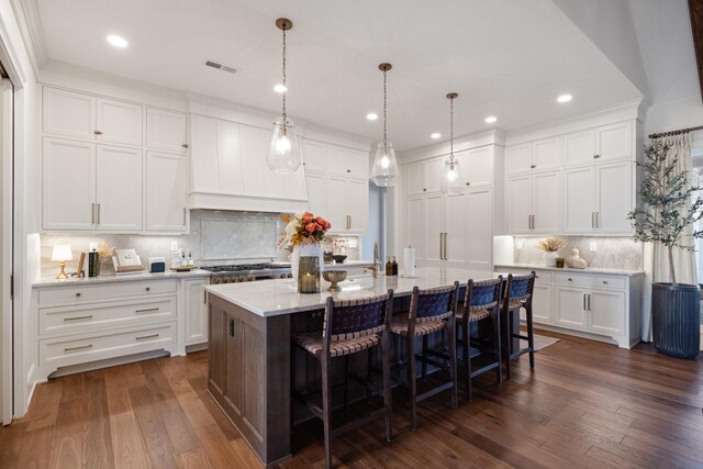 kitchen featuring dark wood-style floors, white cabinets, stainless steel gas cooktop, and a kitchen breakfast bar