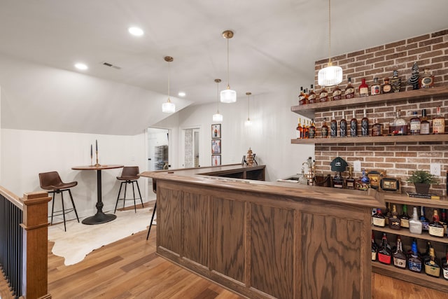 bar featuring lofted ceiling, light wood-style flooring, brick wall, visible vents, and indoor wet bar