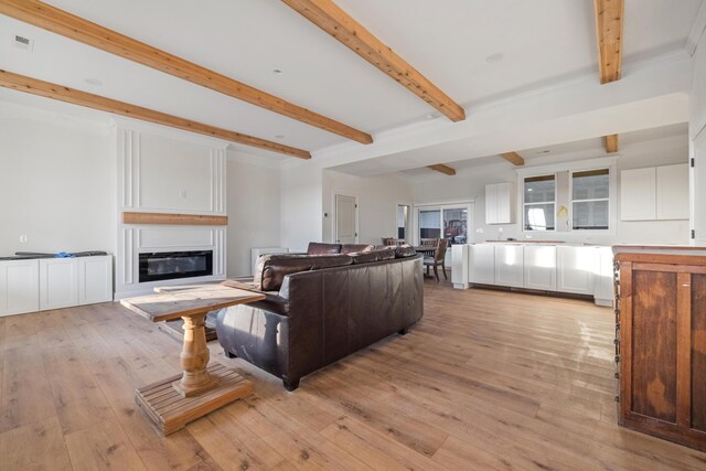 living area with a glass covered fireplace, visible vents, beamed ceiling, and light wood-style flooring