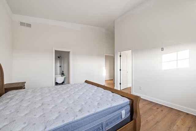 bedroom featuring a towering ceiling, wood finished floors, visible vents, and baseboards