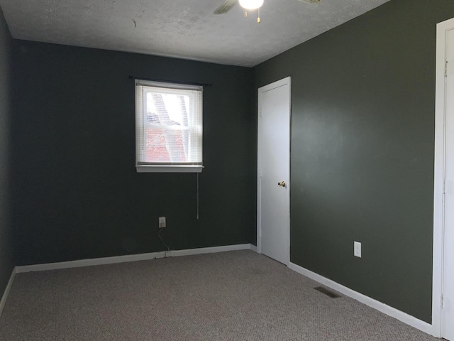 empty room featuring a textured ceiling, carpet flooring, a ceiling fan, visible vents, and baseboards