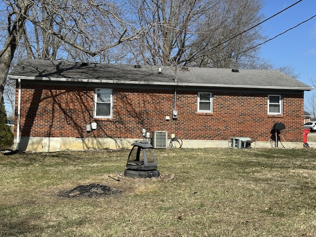 back of house with brick siding, a lawn, central AC unit, and a shingled roof