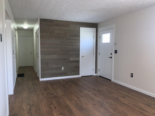 foyer with wooden walls, visible vents, baseboards, dark wood-type flooring, and a textured ceiling