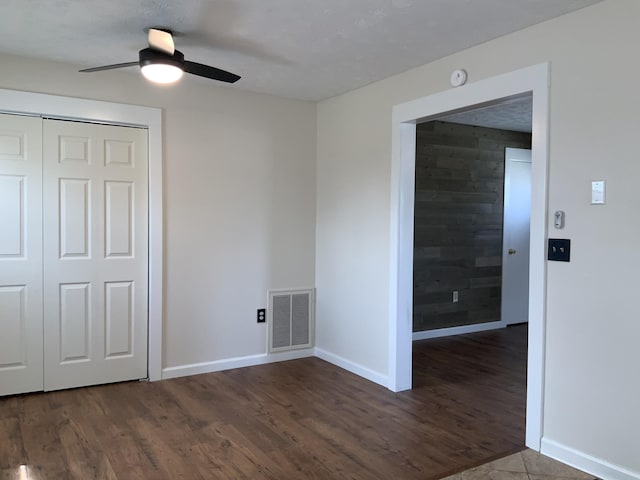 empty room featuring wood walls, wood finished floors, visible vents, and baseboards