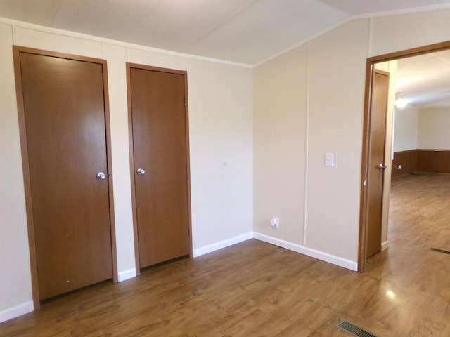 unfurnished bedroom featuring lofted ceiling, wood finished floors, and multiple closets