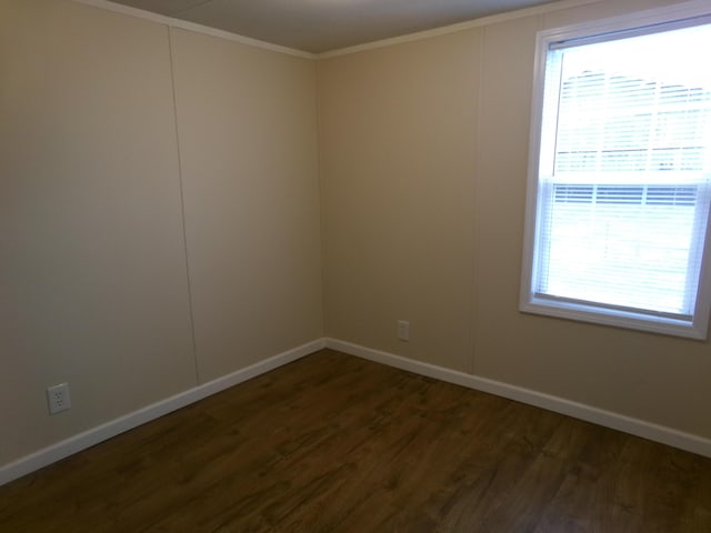 spare room featuring dark wood-type flooring, ornamental molding, and baseboards