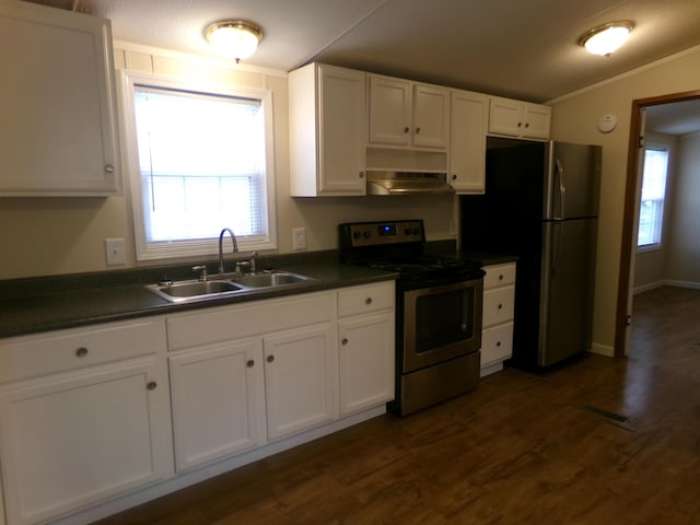 kitchen with stainless steel appliances, dark countertops, white cabinets, a sink, and under cabinet range hood