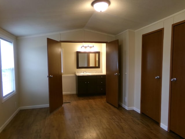 corridor with baseboards, dark wood-style floors, ornamental molding, vaulted ceiling, and a sink