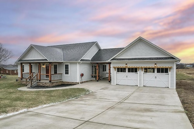 ranch-style home featuring a porch, a shingled roof, an attached garage, a front yard, and driveway