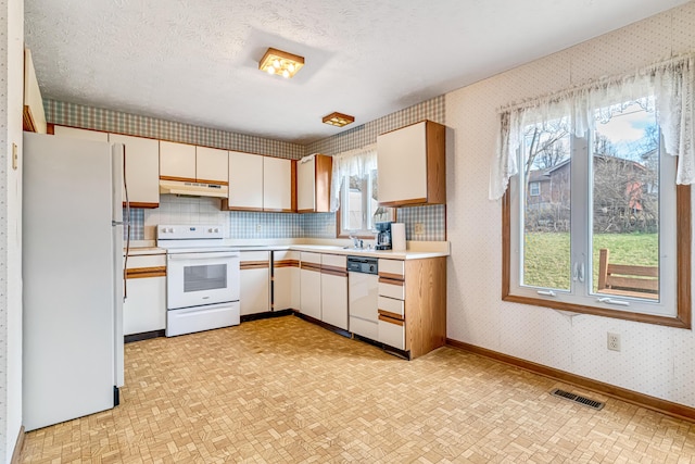 kitchen featuring a textured ceiling, under cabinet range hood, white appliances, visible vents, and wallpapered walls