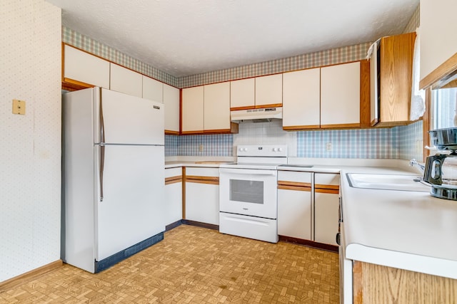 kitchen with a textured ceiling, under cabinet range hood, white appliances, light countertops, and wallpapered walls