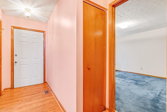 hallway with light wood-style floors, visible vents, a textured ceiling, and baseboards