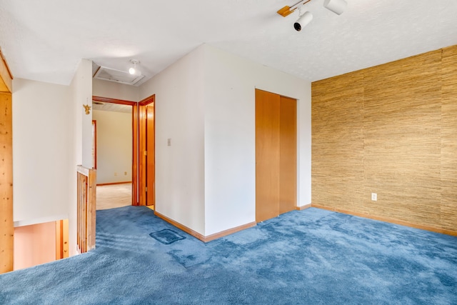 unfurnished room featuring carpet floors, an accent wall, baseboards, and track lighting