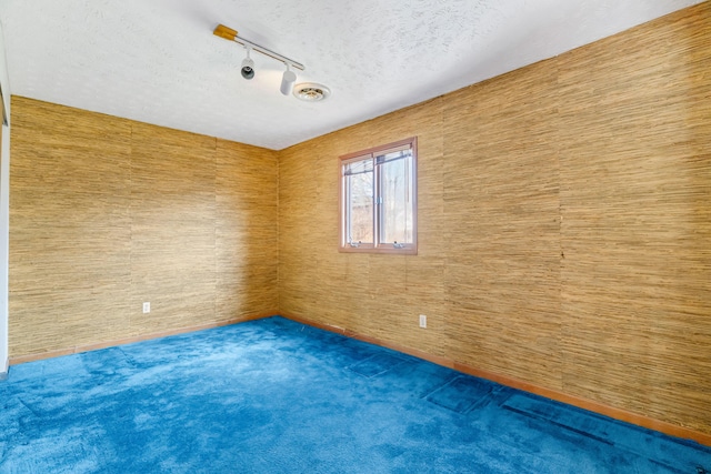 carpeted empty room with rail lighting, visible vents, and a textured ceiling