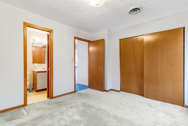 unfurnished bedroom with a textured ceiling, carpet floors, visible vents, baseboards, and a closet