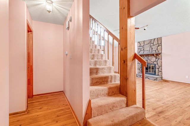 stairway with a fireplace, wood finished floors, and baseboards