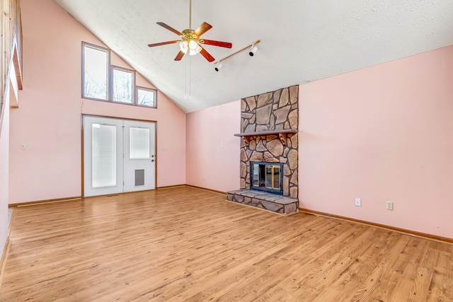 unfurnished living room with a textured ceiling, high vaulted ceiling, a stone fireplace, wood finished floors, and a ceiling fan