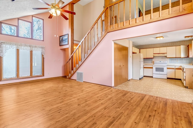 unfurnished living room featuring light wood finished floors, visible vents, a textured ceiling, high vaulted ceiling, and stairs