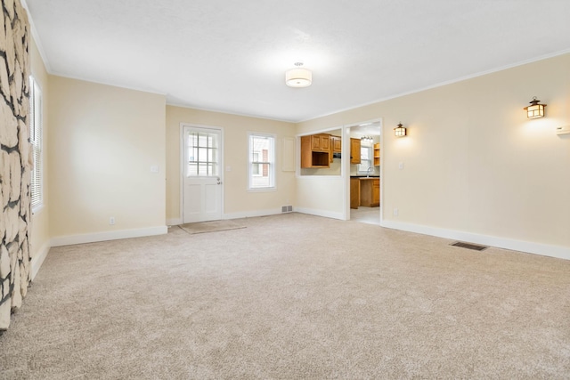 unfurnished living room with visible vents, crown molding, light carpet, and baseboards