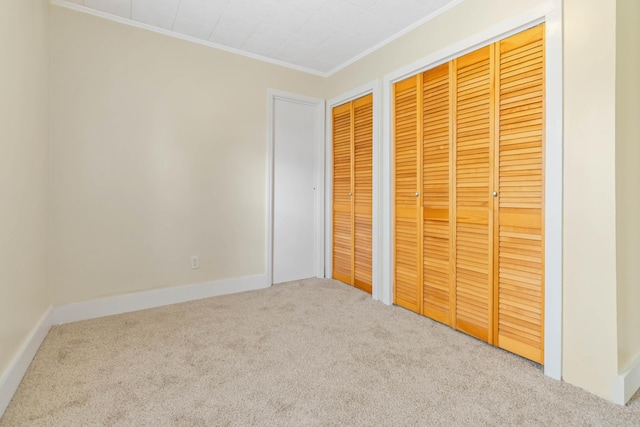 unfurnished bedroom featuring baseboards, ornamental molding, two closets, and carpet flooring