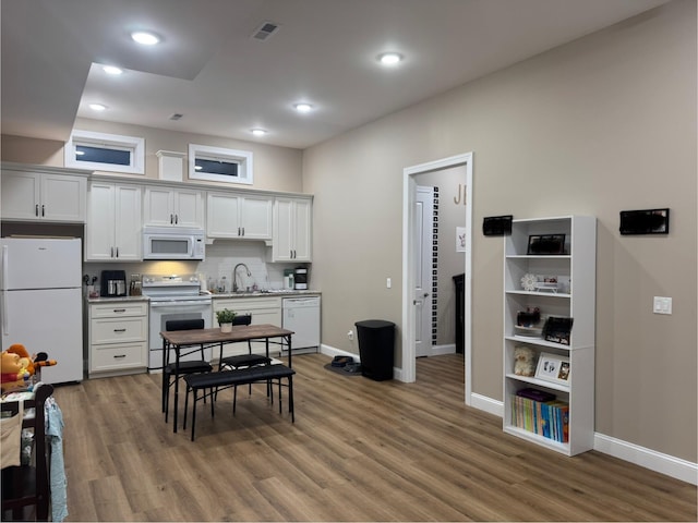 kitchen featuring visible vents, a sink, wood finished floors, white appliances, and baseboards