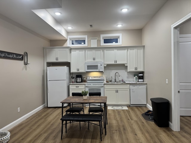 kitchen featuring white appliances, tasteful backsplash, baseboards, wood finished floors, and a sink