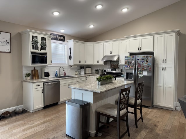 kitchen featuring a breakfast bar area, appliances with stainless steel finishes, vaulted ceiling, under cabinet range hood, and a sink