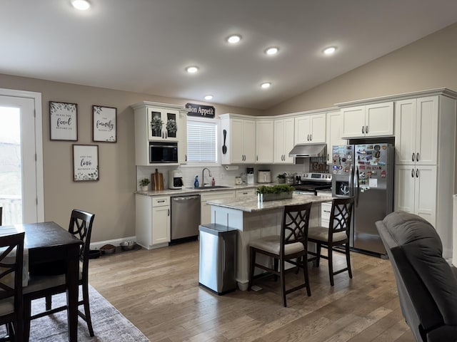 kitchen featuring a breakfast bar area, stainless steel appliances, lofted ceiling, a sink, and under cabinet range hood