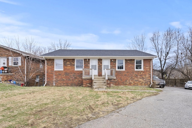 single story home with a shingled roof, a front yard, and brick siding