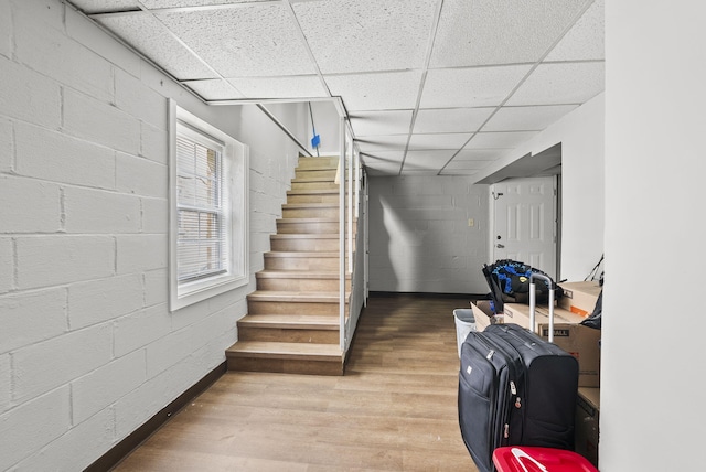 below grade area with a paneled ceiling, stairs, wood finished floors, and concrete block wall