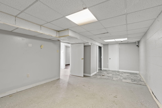 finished basement with concrete block wall, a paneled ceiling, and baseboards