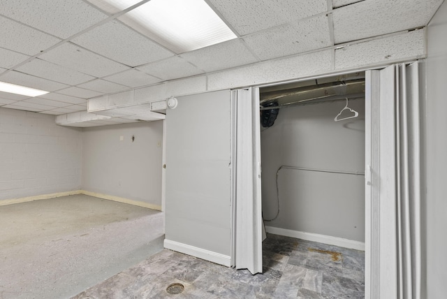 finished below grade area with concrete block wall, baseboards, and a paneled ceiling