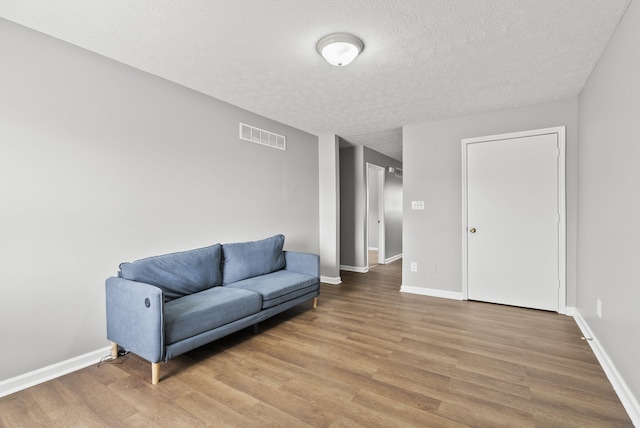 sitting room featuring visible vents, a textured ceiling, baseboards, and wood finished floors