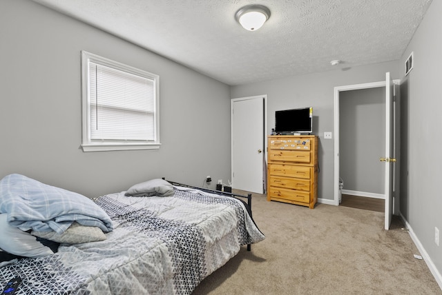 bedroom featuring light carpet, visible vents, baseboards, and a textured ceiling