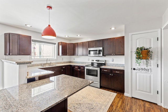 kitchen with dark brown cabinetry, decorative light fixtures, dark wood finished floors, stainless steel appliances, and a sink