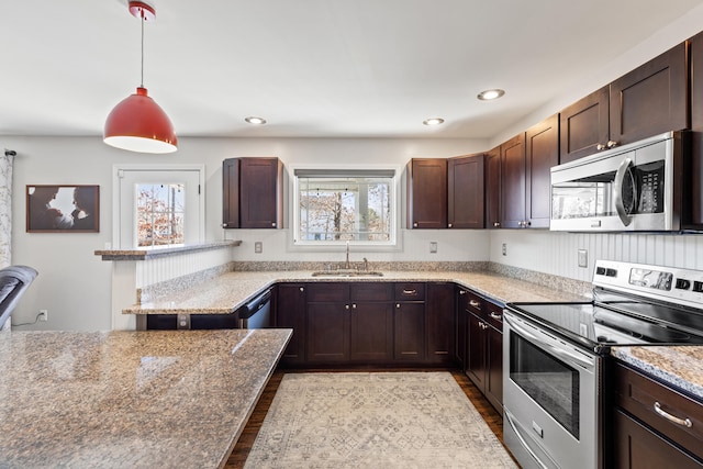 kitchen with wood finished floors, a sink, stainless steel appliances, dark brown cabinetry, and pendant lighting