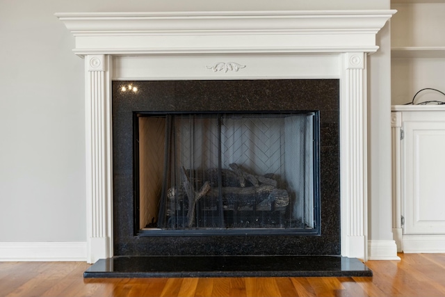 interior details featuring a fireplace with raised hearth, baseboards, and wood finished floors