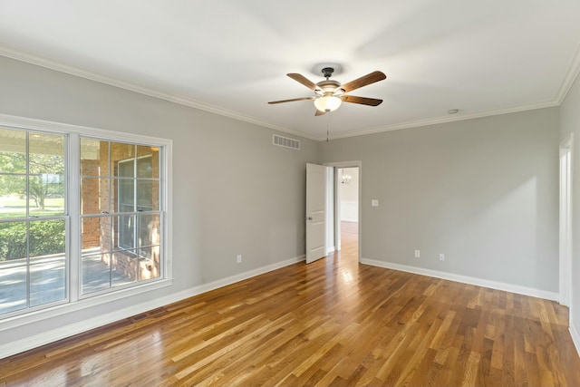 empty room with crown molding, wood finished floors, visible vents, and baseboards