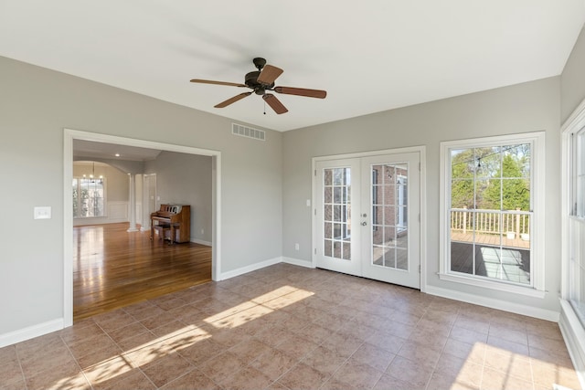 unfurnished room with a wealth of natural light, french doors, ceiling fan with notable chandelier, and visible vents