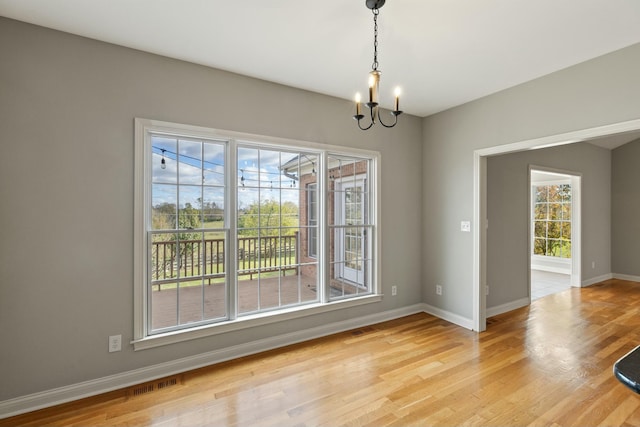 unfurnished dining area with a chandelier, light wood-type flooring, visible vents, and baseboards