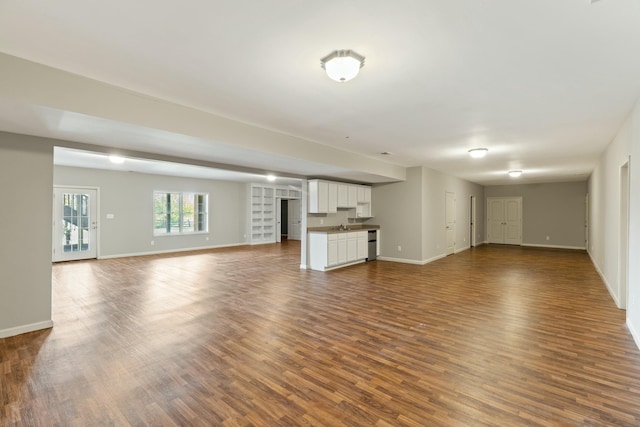 unfurnished living room featuring dark wood-style flooring, a sink, and baseboards