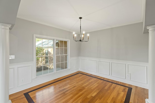 unfurnished dining area featuring a wainscoted wall, decorative columns, a chandelier, and wood finished floors