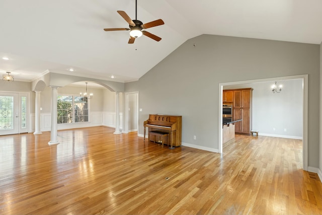 unfurnished living room with arched walkways, ceiling fan with notable chandelier, a wainscoted wall, light wood-type flooring, and ornate columns